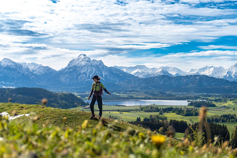 Person mit Wanderrucksack auf einem grünen Hügel, dahinter ein See und schneebedeckte Berggipfel. Person mit Wanderrucksack auf einem grünen Hügel, dahinter ein See und schneebedeckte Berggipfel.
