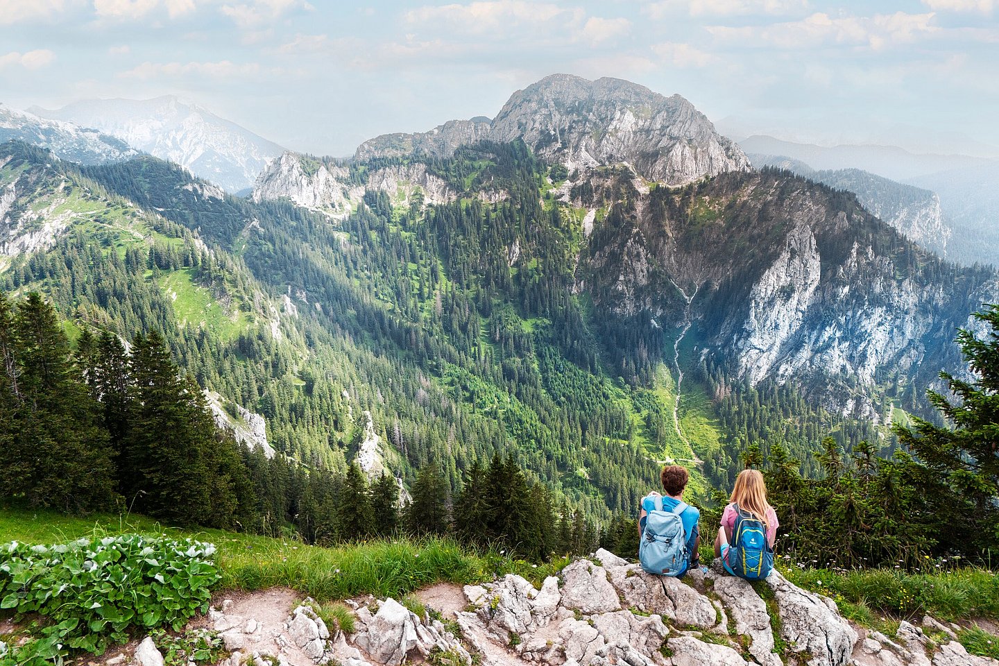 Zwei Wanderer sitzen am Wegesrand und schauen in die Bergwelt