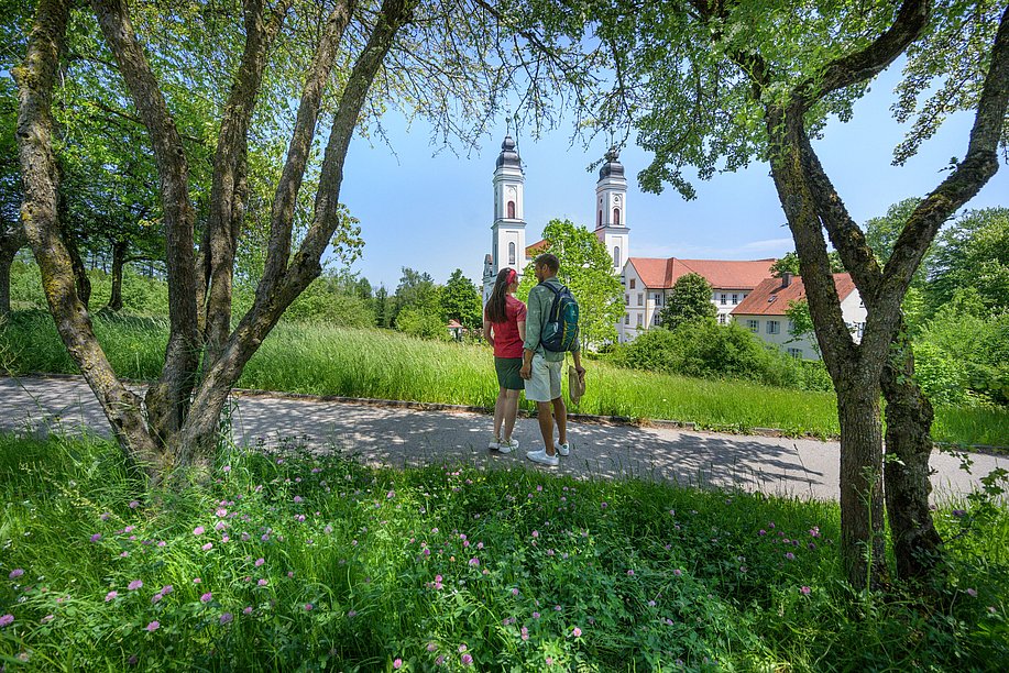 Zwei Personen gehen im Grünen spazieren, im Hintergrund eine Kirche