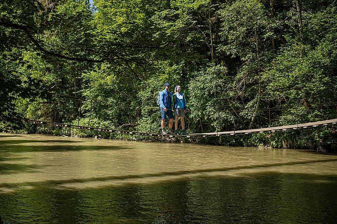 Zwei Personen auf einem Hängesteg über einem Fluss Zwei Personen auf einem Hängesteg über einem Fluss